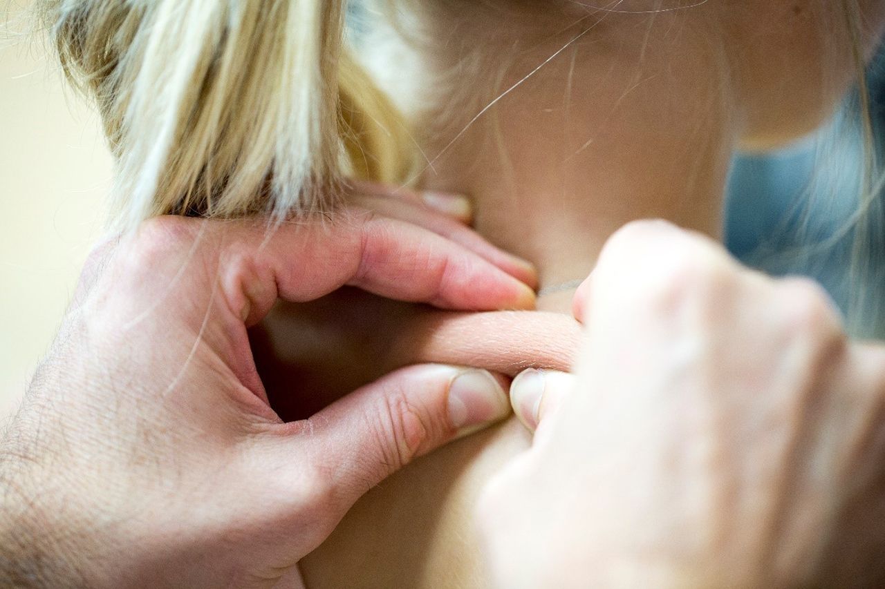 Hände drücken auf einen Akupressurpunkt am Nacken einer Person mit blonden Haaren